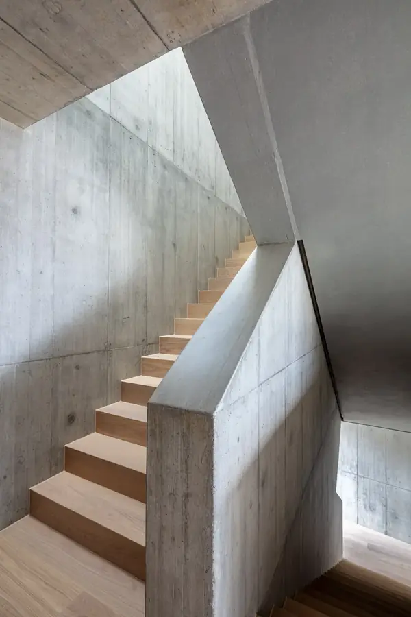 Holztreppe zwischen Sichtbetonwänden mit Oberlicht