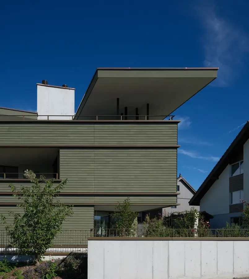 Mehrfamilienhaus mit grüner Holzfassade und weit auskragendem Dach