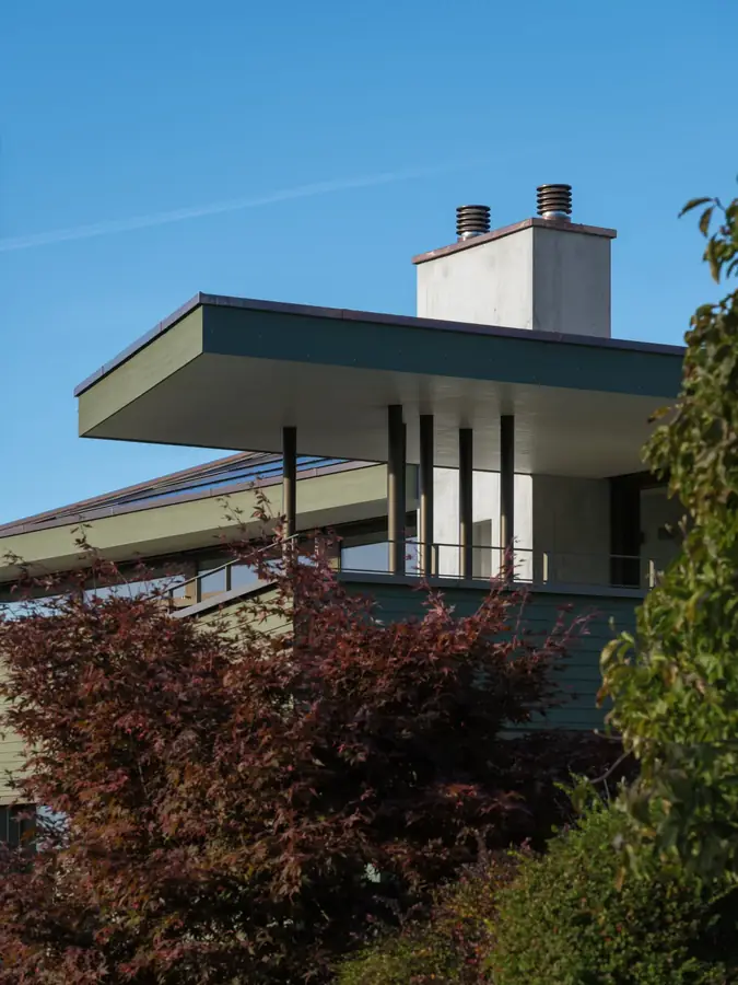 Dachvorsprung über Stützen vor einer grünen Holzfassade